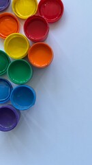 Open colorful paint jars on white background arranged in rainbow palette order. Art supplies, bright gouache colors, creativity and painting concept. Top view with copy space.