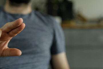 Close-up of a man's hand making a gesture, wearing a simple grey t-shirt.  Neutral background.