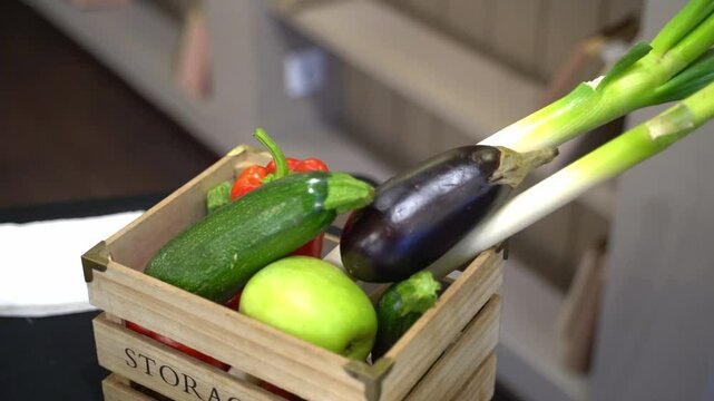 Wooden decorative mini box with fresh vegetables - leeks, zucchini, apples, tomatoes stands on a black table