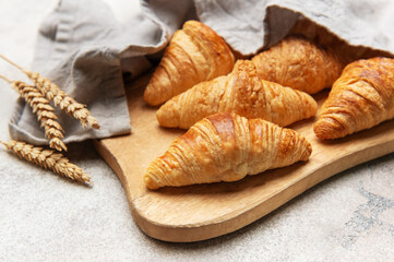 Freshly baked croissants resting on wooden cutting board with wheat stalks