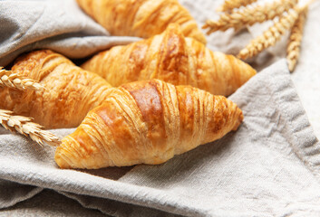 Freshly baked croissants resting on a linen cloth with wheat stalks