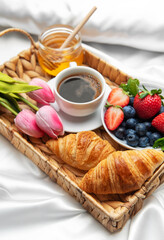 Romantic breakfast in bed with coffee, croissants, berries, honey and tulips