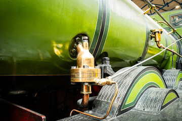 Shallow focus of a brass, steam valve fitting on a green painted, old steam powered locomotive within a, North Yorkshire railway museum. The high pressure brass relief valve can be seen.