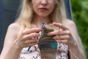 Girl with blonde hair crocheting close up outdoors