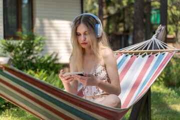 Caucasian girl 20 years old with headphones relaxing in a hammock and watching movie on mobile phone
