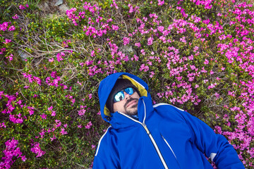 Hiker relaxing in colorful wildflower meadow, surrounded by bright pink blooms while wearing protective outdoor gear and mirrored sunglasse