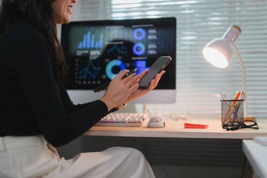 Businesswoman analyzing financial charts on computer and smartphone, working with data