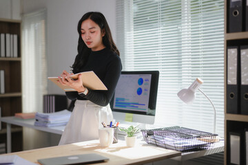 Businesswoman taking notes in modern office with computer showing charts