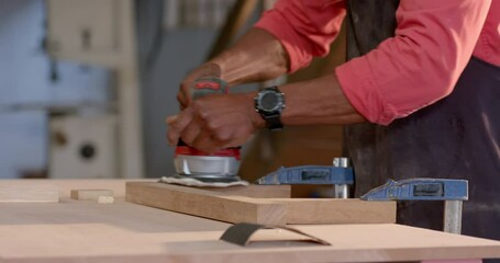 Senior African American man operating power tool on wood board in woodshop, with apron, copy space - Powered by Adobe
