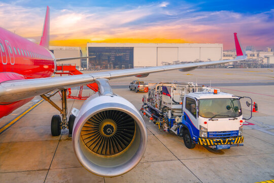Airplane being preparing ready for takeoff in international airport. The fuel truck has arrived and is standing nearby wing, against the backdrop of aerospace hangar