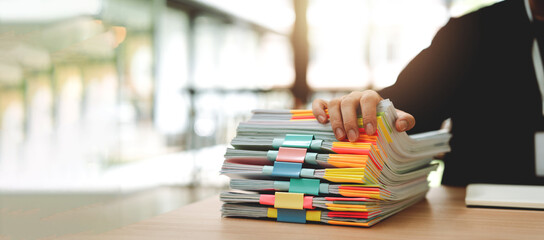 Portrait of an employee working with a large number of documents, searching for documents, accounting of income and expenses, tax records and checking documents on a desk in an office.