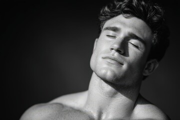 Close-up portrait of a young man relaxing with eyes closed in dramatic black and white lighting highlighting facial features and strong jawline conveying a moment of serenity and self-reflection