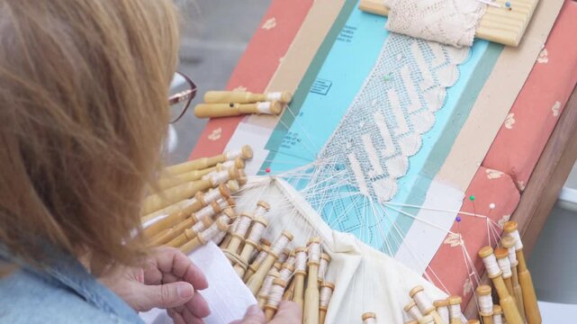 Bobbin lace making in Galicia, Spain &mdash; traditional lace-producing art. An elderly woman crafting beauty in a modern-day Spanish town square.
