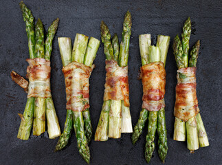 
Grilled green asparagus wrapped bacon on a dark background, top view