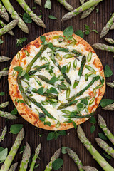 Pizza with green asparagus and herbs on a wooden background, top view
