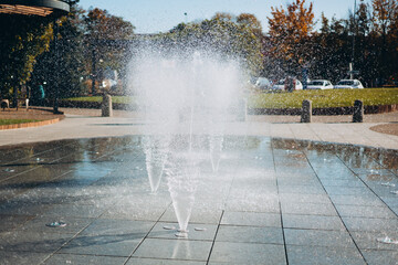 Water droplets spread from the fountain in the air. Splashing water from a fountain in the park. Vertical fountain jets in the sidewalk on the square in the city park.