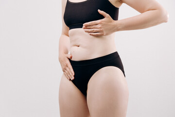 Fototapeta premium Woman in black underwear holds her stomach, expressing discomfort and pain, highlighting the emotional and physical aspects of health struggles
