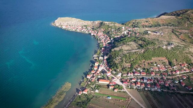 Forward drone shot over Lin village in Pogradec, Albania, revealing red-roof houses along Lake Ohrid, a coastal peninsula, and the site of Europe&rsquo;s most ancient known settlement.