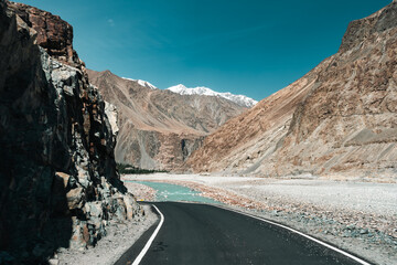 A winding road climbs through the rugged snowy slopes of Ladakh high-altitude mountains, capturing...