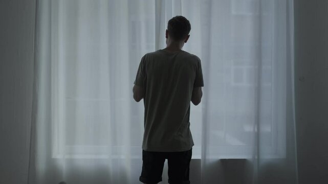 Agoraphobic man staring out the window, afraid to leave home. Mental health struggle with fear of open spaces.