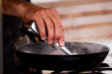 A skilled chef carefully fries bacon in a black cast iron pan over an open flame. The image captures the essence of culinary expertise and the sizzling process that enhances the flavors of this savory