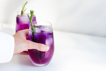 An unrecognizable female hand takes a purple cocktail from the table.