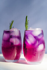 Glasses with freshly made purple cocktails with ice and rosemary stand on table.