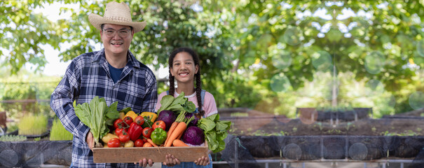 Fototapeta premium Farmer holding wooden box full of fresh vegetables. Basket with vegetable. Man and Daughter holding big box with different fresh farm vegetables.