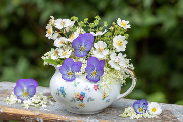 Blumen-Arrangement mit blauen Hornveilchen (Viola cornuta), Rosen und Holunderblüten in vintage Sauciere