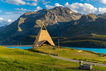A pyramid shaped church stands on a green lawn in the warm sunset light in Mont Cenis, France.