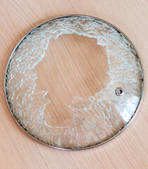 damaged glass lid with metal rim, shattered with pieces missing, is sitting on light colored wooden surface