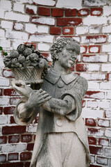 Fototapeta premium Statue of a young boy carrying a basket of fruits in a garden with a brick wall background