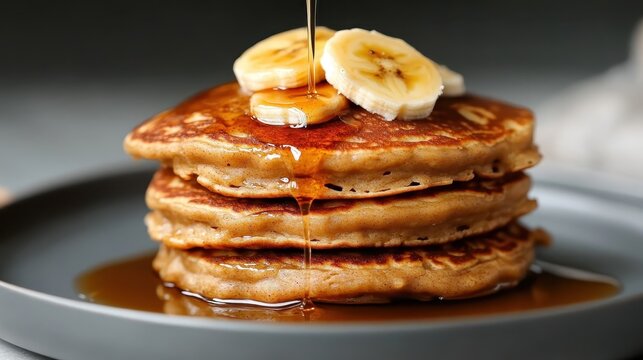 A delicious stack of fluffy pancakes topped with fresh bananas and drizzled with syrup, making it an enticing breakfast option that tantalizes the senses.