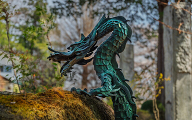Colorful oxidized green and azure scales on a copper dragon water spout mounted on a stone purification fountain covered in yellow, orange, and green moss at a Buddhist temple in Yamanashi Prefecture,