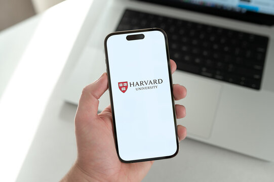 Student holding smartphone with harvard university logo displayed on screen