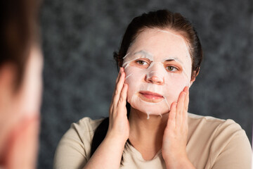 Female applying moisturizing face mask in bathroom. Beauty routine. International Self Care Day.