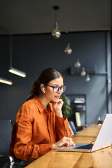 Busy latin hispanic young business woman working on laptop computer sitting at office desk. Indian entrepreneur manager businesswoman using pc for communication, learning at workplace. Vertical