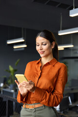 Smiling Latin Hispanic mature female businesswoman holding smartphone in office trading app, working online. Young Indian business woman manager ceo using cell phone mobile application. Vertical