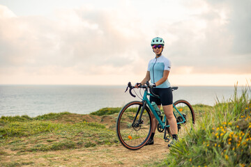 Obraz premium Latin cyclist woman enjoying the sunrise by the sea with her gravel bike