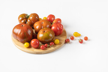 Red, green, yellow and striped tomatoes on a wooden cutting board on a gray background. Healthy food, fresh healthy vegetables from the garden