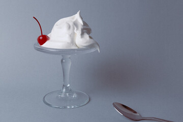 Whipped cream dessert garnished with a cherry on a glass pedestal