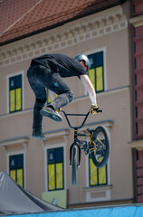 BMX athlete in black attire and helmet performs a dynamic mid-air trick against the backdrop of...