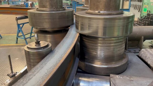 Close-up view of an industrial bending machine in action, shaping steel profiles and pipes with precision. Ideal for themes of manufacturing, heavy industry, and metalworking processes.