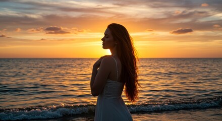 Fototapeta premium Serenity by the Ocean Sunset - A woman stands peacefully by the ocean, enjoying a beautiful sunset. The symbolizes tranquility, peace, hope, reflection, and escape