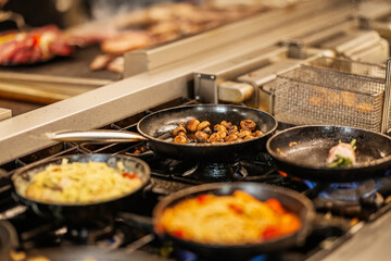 Close-up of multiple frying pans cooking gourmet meals in a professional kitchen, showcasing dynamic culinary preparation and sizzling ingredients.