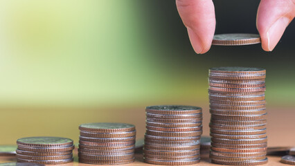 Man hand holding coin and put on the stacked coin on the table in concept of account for money saving, financial planning and retirement plan.