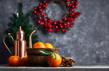 Still life with copper pitcher teapot and ripe fresh orange tangerine fruits in a wooden, barrel-shaped rustic bowl on bark wood table. Grunge stone wall berries wreath Christmas tree on background.