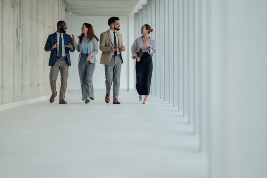 Diverse businesspeople walking and talking in modern office hallway