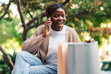 Happy shopper talking on mobile phone, checking shopping bags in park