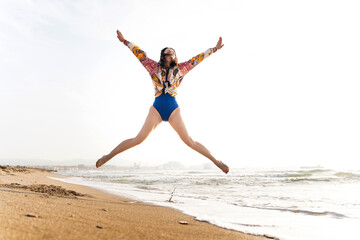 Obraz premium Woman jumping on the beach expressing freedom and happiness at sunrise